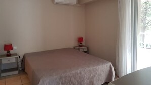 Un dormitorio con una cama, dos mesitas de noche con lámparas, aire acondicionado y una ventana con cortinas.