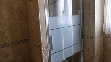 Un baño con ducha de vidrio, inodoro y felpudo.