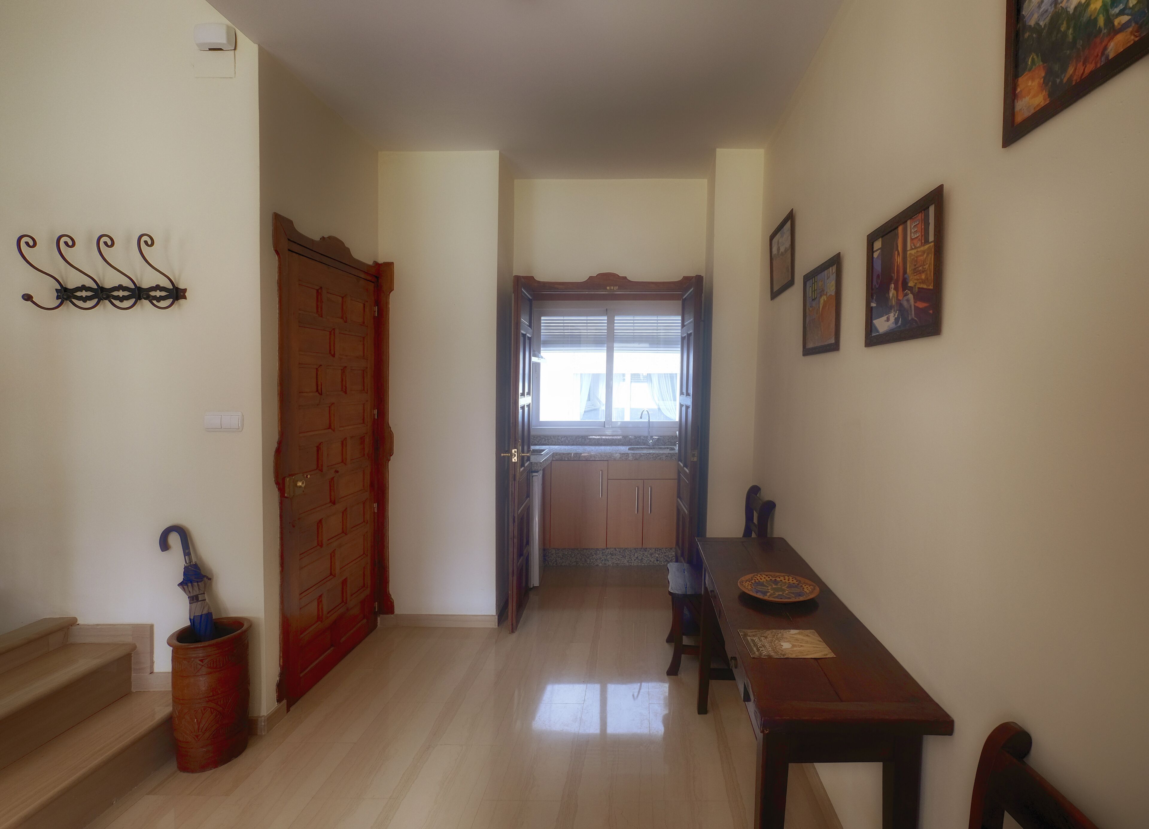 A hallway with a wooden door, a dining table with chairs, a window with curtains, and a wall-mounted light fixture.