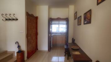 A hallway with a wooden door, a dining table with chairs, a window with curtains, and a wall-mounted light fixture.
