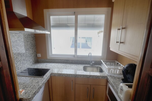 A compact kitchen with granite countertops, a built-in stove, a sink, and wooden cabinets.