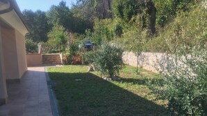 Un chemin pavé mène à une zone herbeuse bordée d’un muret en pierre et d’un petit arbre.