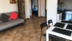 Un salon avec un canapé, une table à manger avec des chaises, un coin cuisine équipé d’une cuisinière et d’un four, et une porte en arc donnant sur une autre pièce.