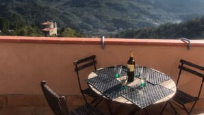 Une table ronde avec quatre chaises, une bouteille de vin et deux verres, le tout placé sur un balcon donnant sur un paysage montagneux.
