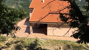 Une maison avec un toit recouvert de tuiles rouges, une petite dépendance attenante et une vue sur un paysage vallonné.