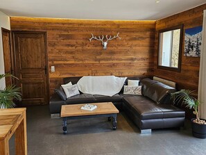 A cozy living room with a wooden wall, a leather sofa, a coffee table, and a deer head decoration. - 4★ Duplex in La Clusaz Center, 8 guests, 3 bedrooms (La Clusaz)