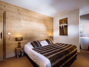A bedroom with a wooden wall, a bed with a fur throw, bedside lamps, and a painting. - 4★ Duplex in La Clusaz Center, 8 guests, 3 bedrooms (La Clusaz)