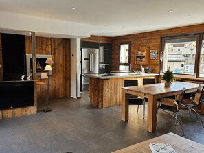 Une cuisine moderne avec des éléments en bois, des appareils en acier inoxydable et un coin repas comprenant une table et des chaises en bois.