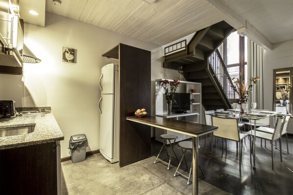 A modern kitchen with a built-in refrigerator, a dining area with a table and chairs, and a staircase leading to an upper level.