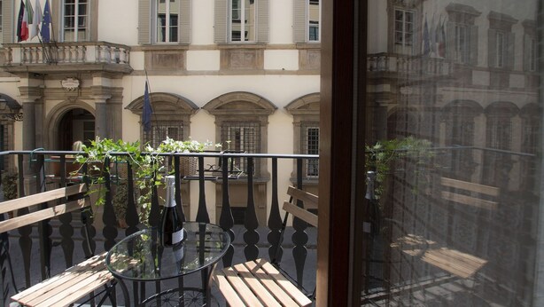 A balcony with a glass table and wooden benches, overlooking a building with multiple windows and flags. - Spacious and charming apartment in the heart of Florence (Firenze, Italia)