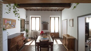 A dining area with a wooden table, chairs, and a red chair. There is a corkboard with various items pinned to the wall, a radiator, and a window with curtains. - Spacious and charming apartment in the heart of Florence (Firenze, Italia)