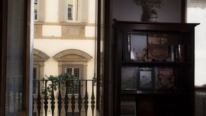 A view from a balcony with a potted plant, a bookshelf with books, and a building with arched windows in the background. - Spacious and charming apartment in the heart of Florence (Firenze, Italia)