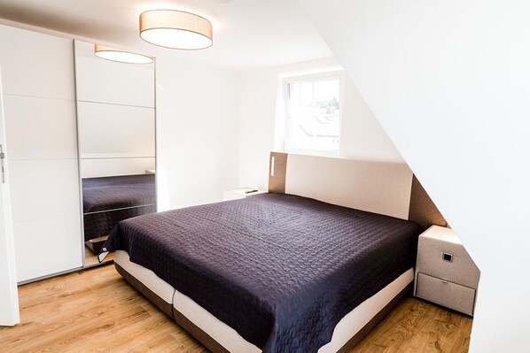 A bedroom with a bed, a nightstand, a mirror, and a window.