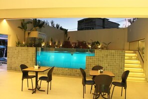 An outdoor pool area with a glass barrier, chairs, and tables.