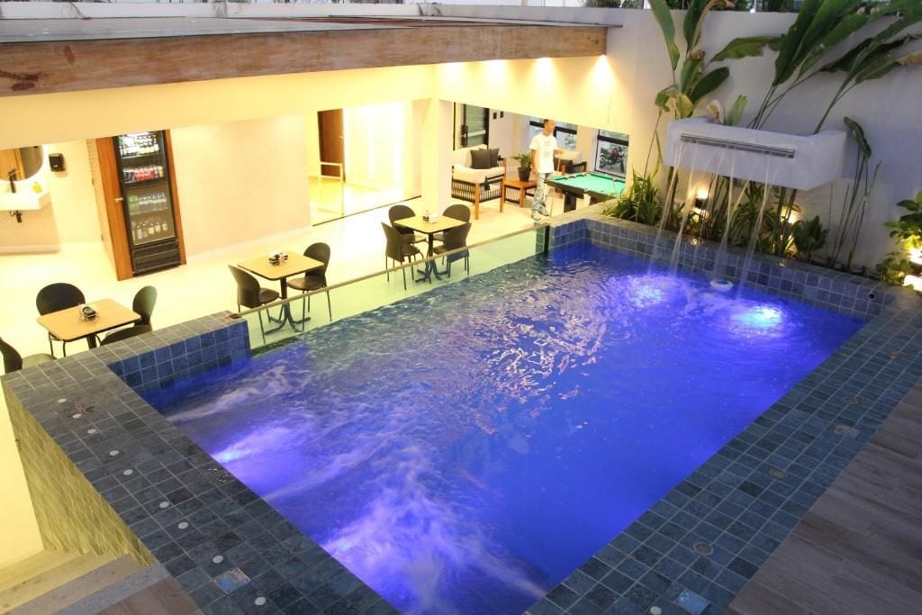 An indoor swimming pool with a blue-lit water feature, surrounded by seating and a bar area.