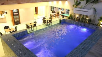 Une piscine intérieure dotée d’un élément décoratif aquatique illuminé de lumière bleue, entourée de sièges et d’un espace bar.