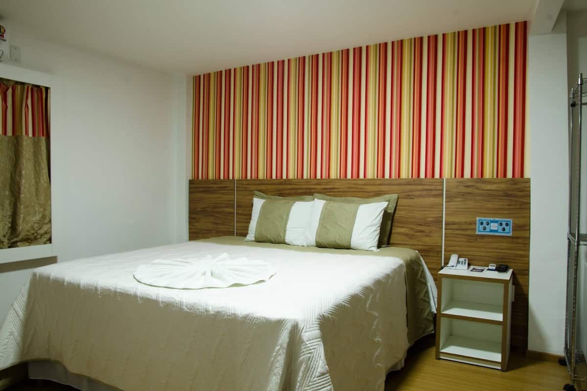 Hotellihuone, jossa on sänky, yöpöytä, jossa on puhelin ja pieni lamppu, raidallinen seinä ja puinen pääty.