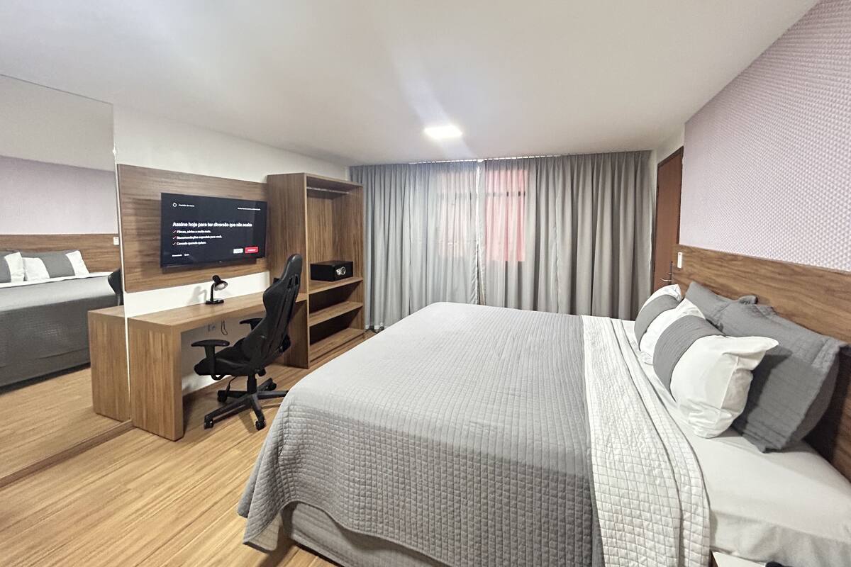 Hotellihuone, jossa on sänky, työpöytä, tuoli, televisio ja ikkuna, jossa on verhot.
