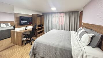 Habitación de hotel con cama, escritorio, silla, televisor y ventana con cortinas.