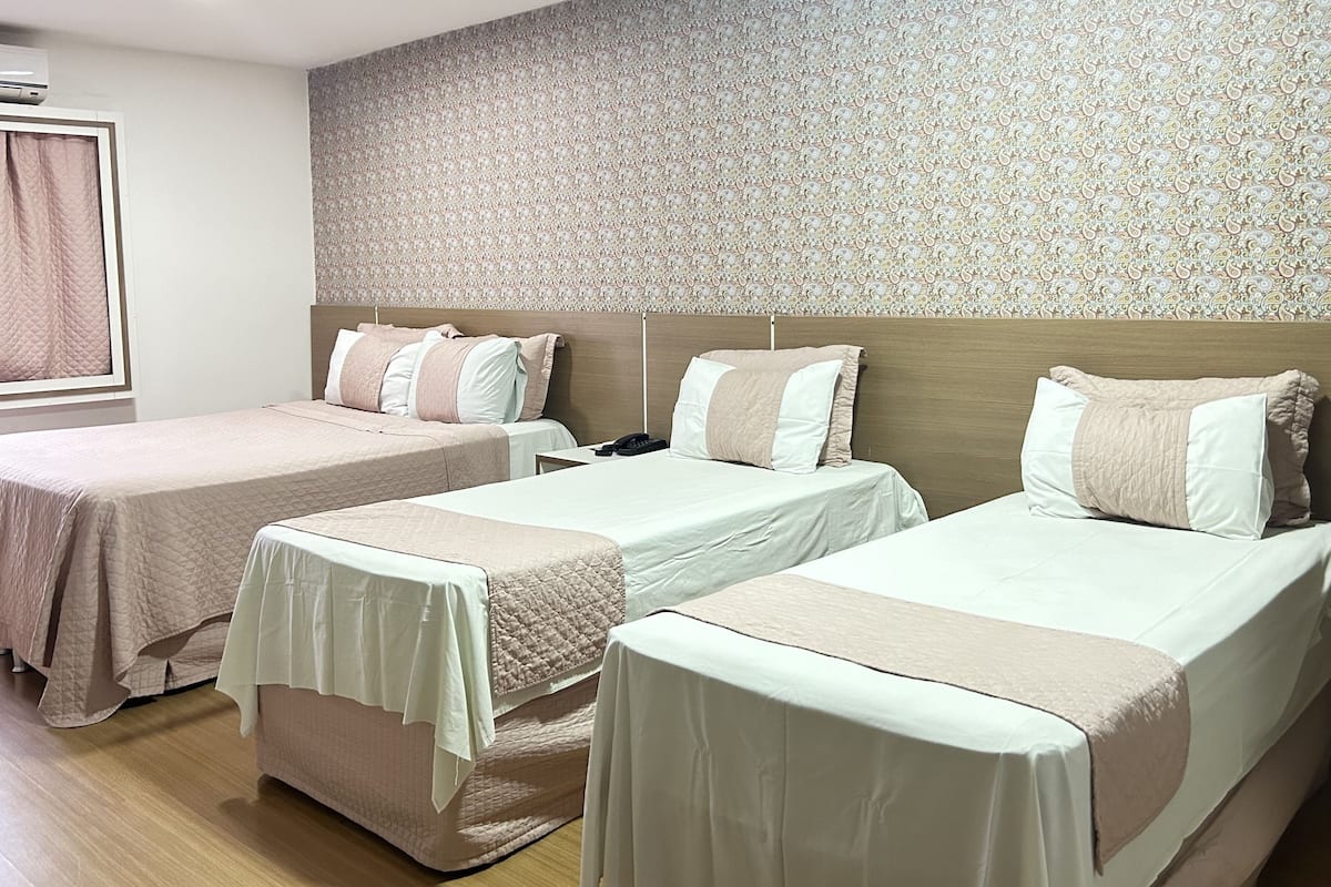 Hotellihuone, jossa on kaksi erillistä sänkyä, puinen pääty, kuvioitu tapetti ja ikkuna, jossa on verho.
