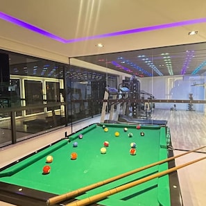 A pool table with balls, a billiard cue, and a glass partition.