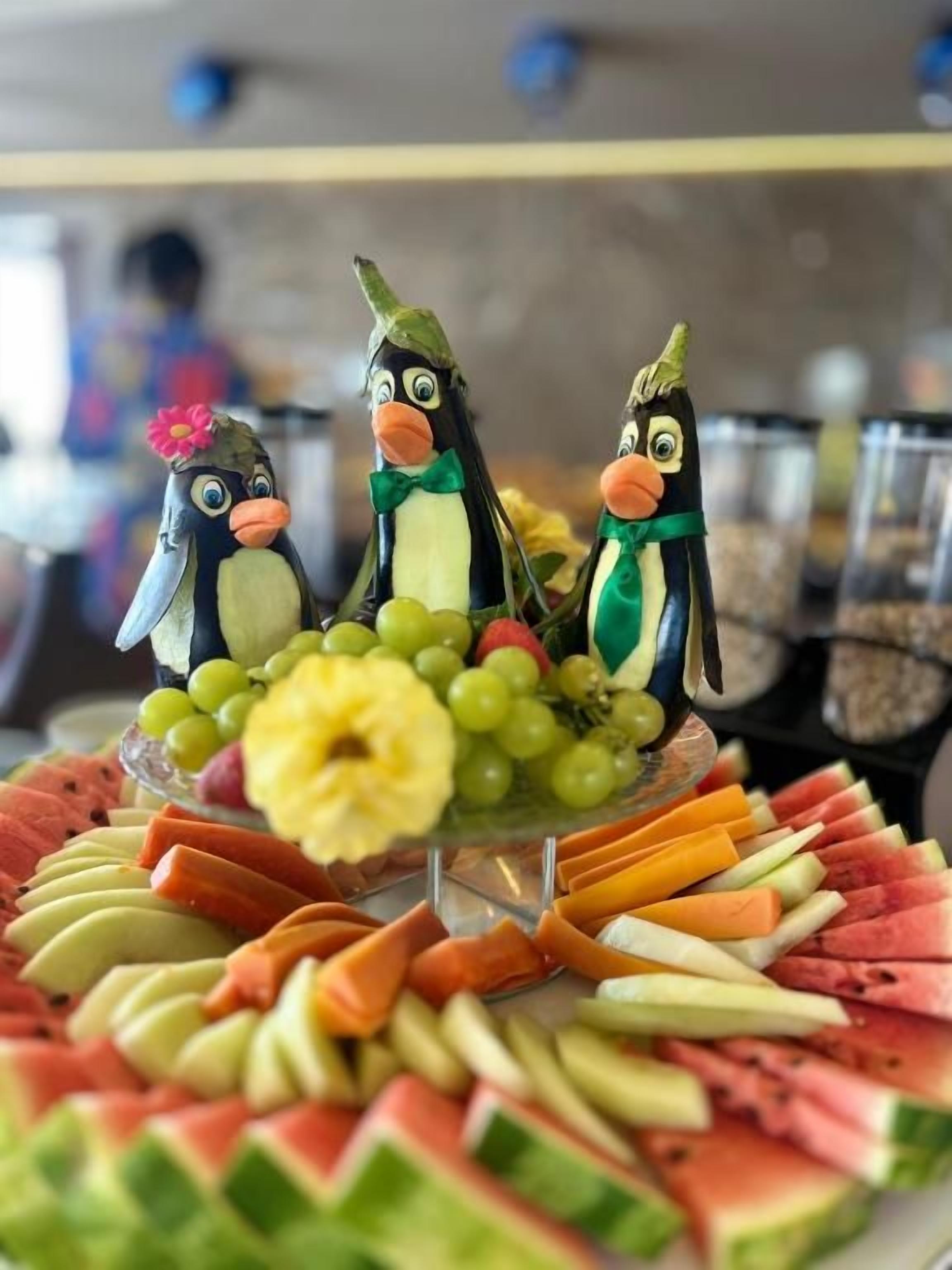 A fruit platter with penguin decorations and a variety of fruits.