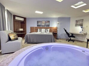 A hotel room with a bed, a sofa, a desk, a chair, a desk lamp, and a bathtub. - Belavista Hotel (Itaberaba)