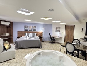 A modern hotel room with a bed, a desk, a chair, a desk lamp, a vanity, a bathtub, and a wardrobe. - Belavista Hotel (Itaberaba)