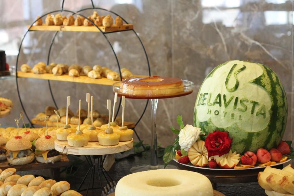 Un bufé con diversos alimentos, incluyendo una sandía como pieza central con la marca 'Delavista Hotel'.