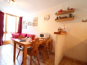 Un comedor acogedor con una mesa y sillas de madera, microondas y tetera roja. Hay repisas sobre la mesa que contienen diversos utensilios de cocina.
