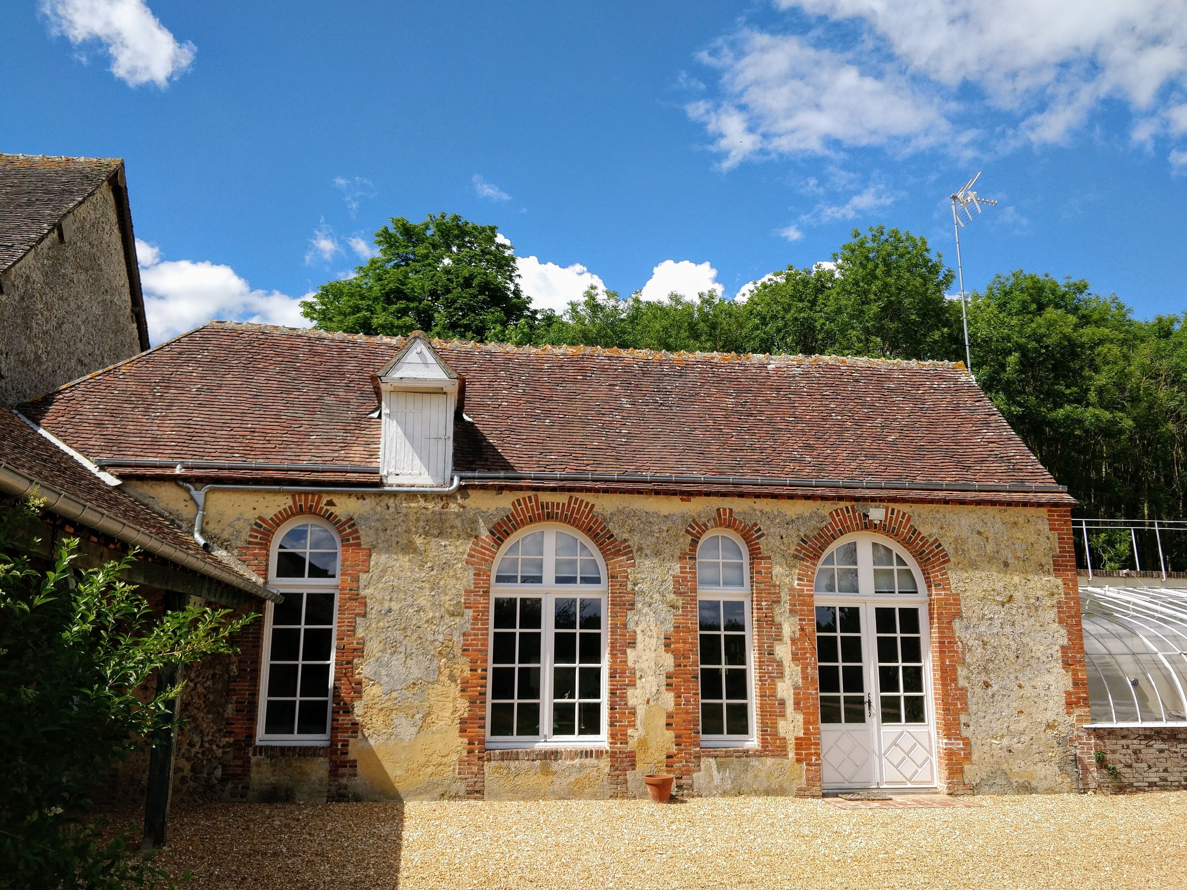A rustic building with a tiled roof, arched windows, and a small attached structure with a white door.