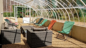 A covered outdoor seating area with wicker furniture and a greenhouse structure. - the Grand Potager, a very beautiful calm and preserved environment (Mittainvilliers-Vérigny)