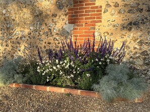 Un jardin agrémenté de lavande et de fleurs blanches, un mur de pierre et une construction en briques.