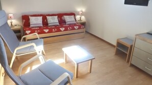 A cozy living room with a red sofa, two armchairs, a small table, and a TV mounted on the wall. - Central studio in Brides-les-Bains with balcony and WiFi (Brides-les-Bains)