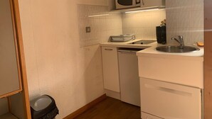 Una cocina compacta con armarios blancos, microondas, lavavajillas y pileta.