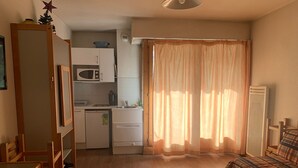 Una habitación compacta con kitchenette, una cama con manta escocesa y un armario de madera.