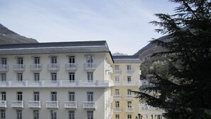Un hotel de varios pisos con balcones, techo plano y montañas al fondo.