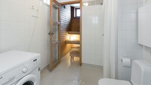 A compact bathroom with a washing machine, a toilet, and a shower area.