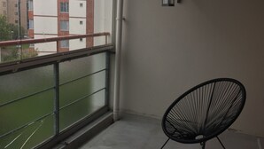A balcony with a zebra-patterned rug, a black chair, and a view of buildings through a glass door.