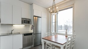 A modern kitchen with white cabinetry, stainless steel appliances, and a dining area with a wooden table and white chairs.