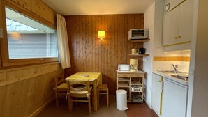A compact kitchen with wooden walls, a small dining table, and basic appliances.