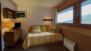 A cozy bedroom with a bed, a desk with a lamp, a radiator, and a window with a view of the outdoors.