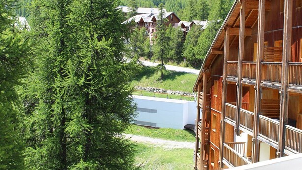 Una cabaña de madera con varios balcones, rodeada de vegetación exuberante y montañas al fondo.
