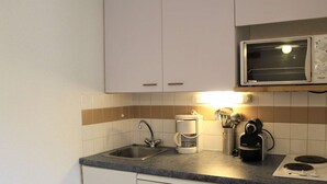 Una cocina compacta con armarios blancos, un microondas integrado, una cafetera y una estufa.