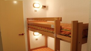 Una cama litera con colchón a rayas, una puerta con picaporte rojo y un aplique en la pared.
