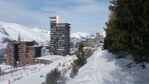 A ski resort with modern buildings, including a tall hotel with a unique rooftop design, surrounded by snow-covered mountains. - Cosy Studio for 2 with Balcony on La Croisette, Ski-In/Ski-Out (Les Menuires)