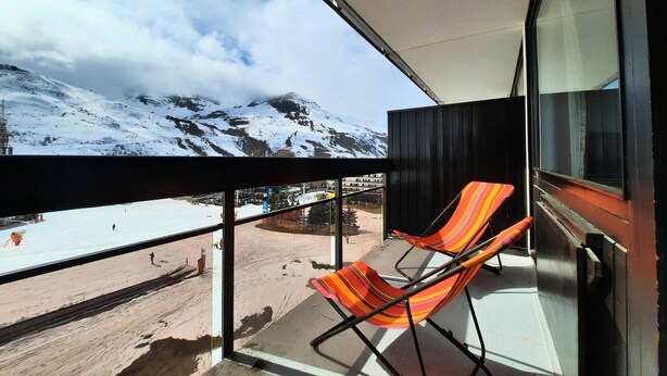 Un balcon avec deux chaises à rayures, une vue sur une montagne enneigée et un ciel dégagé.