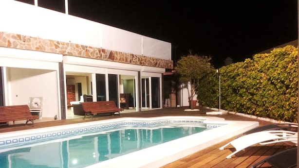 Piscina com deck de madeira, um banco e área coberta com outro banco.