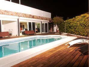 A swimming pool with a wooden deck, a bench, and a covered area with a bench.