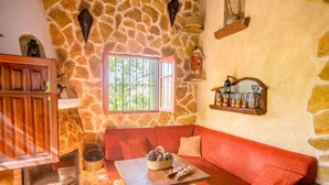 A cozy room with a stone wall, a red sofa, a wooden table, and a fireplace. - Cubo's Jacaranda Rural Cottage / Private Pool / Views (Guaro)